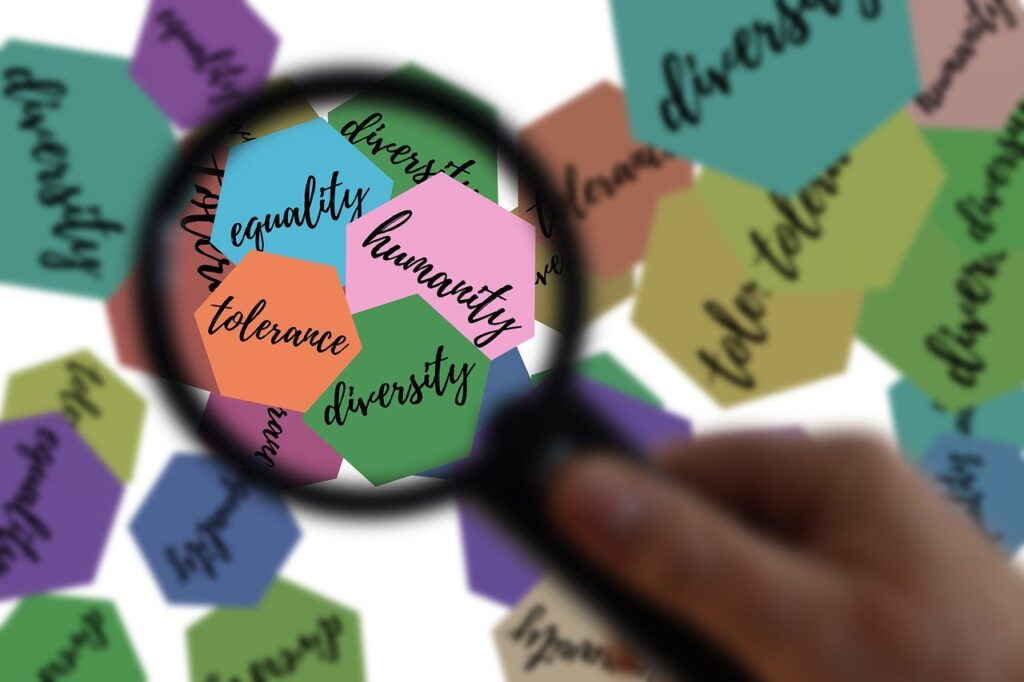 Eine schwarze Lupe, die sich auf bunte Papierschnitte mit Worten tolerance, humanity, diversity und equality fokussiert.